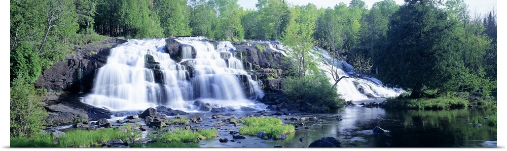 Panoramic photograph on a giant wall hanging of a wide waterfall surrounded by a lush, green forest of trees, in Michigan.