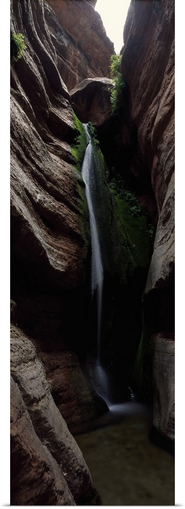 Vertical panoramic photograph of cascading water falling between tall rock formations.