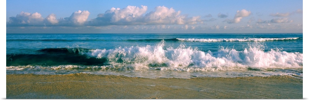 Panoramic photograph of cloudy day at the beach with sea surf crashing onto the sand.