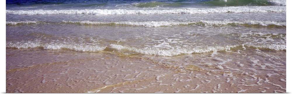 Giant, landscape photograph of small waves rolling onto the shore, covering the sand, in the Gulf of Mexico.