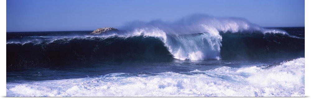 This panoramic beach photograph captures a wave curling and breaking off the shore.