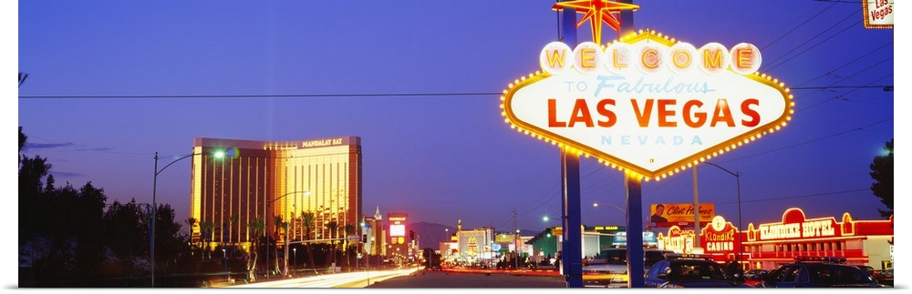 Panoramic photograph of huge neon sign in ""Sin City"" with buildings lit up in the distance at dusk.