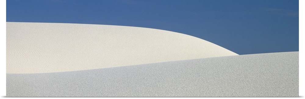 Panoramic photograph of the sloping dunes of White Sands, New Mexico, contrasting with the darker sky, creating a minimali...