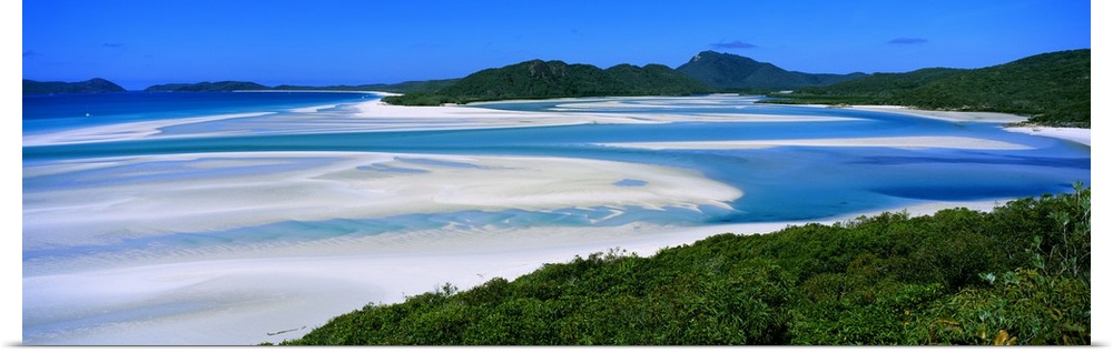 Panoramic view of white beaches and water surrounded by hills and dense forest.