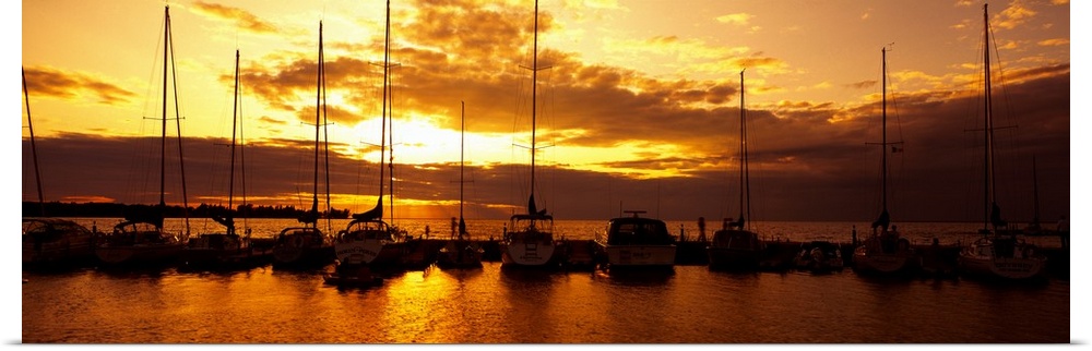 Panoramic photograph of many boats in a line, docked in Egg Harbor beneath a vibrant setting sun, in Door County, Wisconsin.