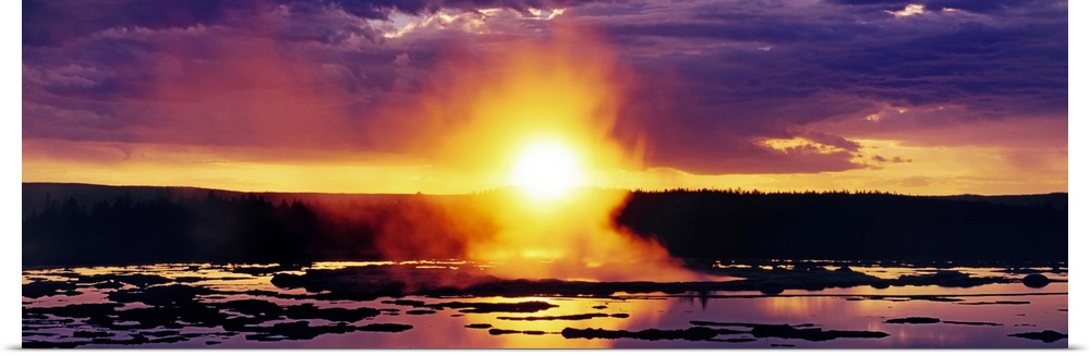 Wide angle shot of the sun setting over Yellowstone as steam billows off the water below.