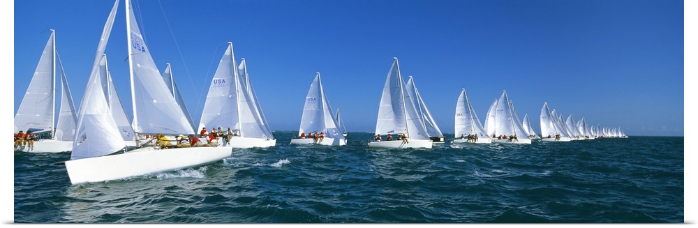 Big, landscape photograph of many white yachts in a line, beneath a blue sky, during a race in the waters of Key West, Flo...