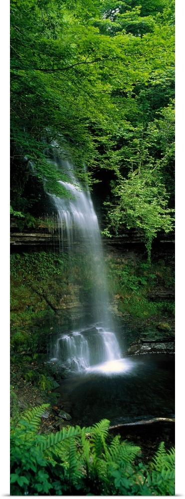 Vertical panoramic photograph of water cascading over a tree covered cliff's edge down to a lagoon.