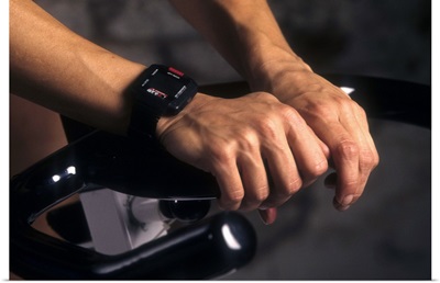 Detail of hands on stationary bike with heart rate monitor watch