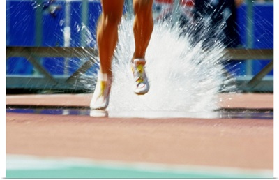 Runners' legs splashing through the water jump of a track and field steeplechase race
