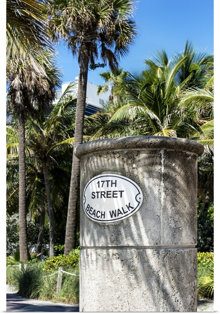 A stone sign for the Beach Walk in Miami, shaded by palm trees.