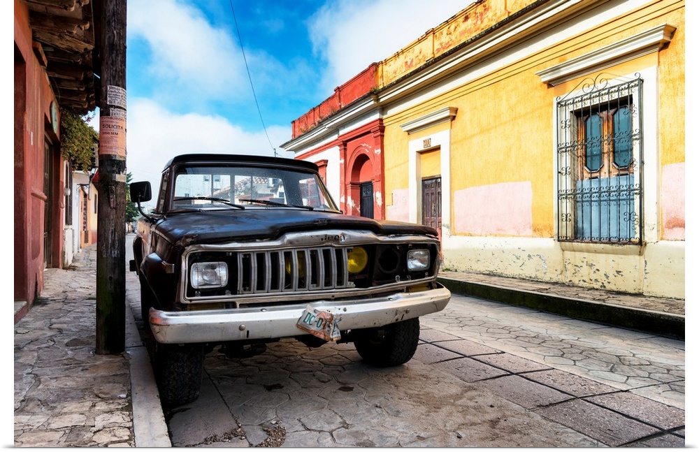 Photograph of an old black Jeep parked on the side of a colorful street in Mexico. From the Viva Mexico Collection.