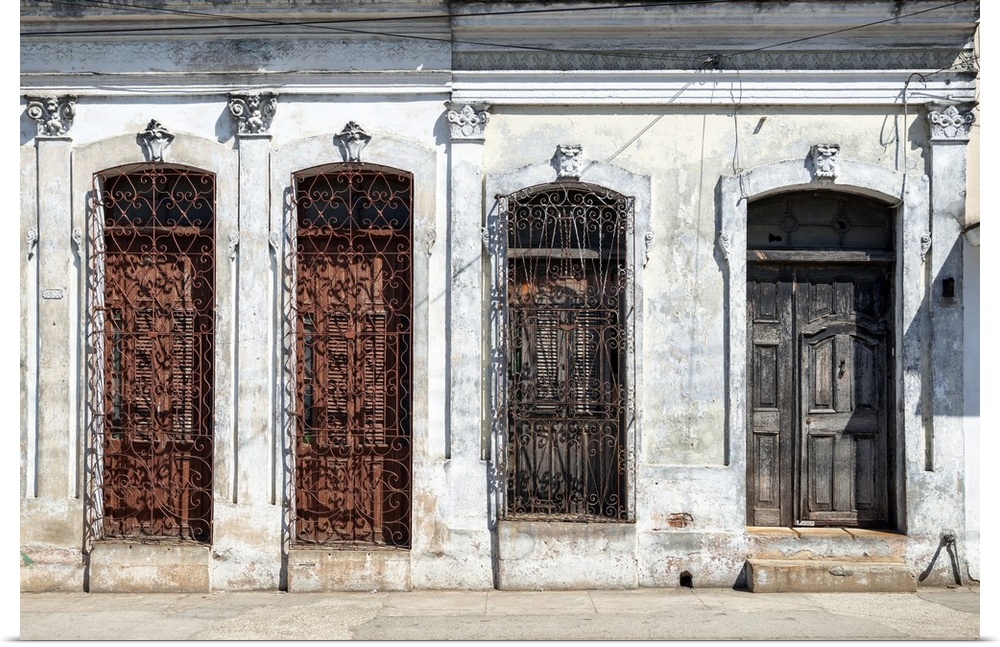 Photograph of an aged Cuban facade with windows and a wooden door.