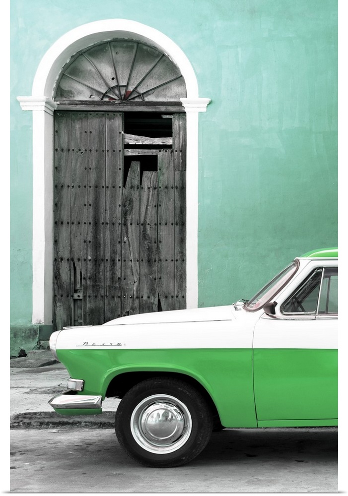 Photograph of the front of a vintage green and white car outside of a green building with a broken wooden door.