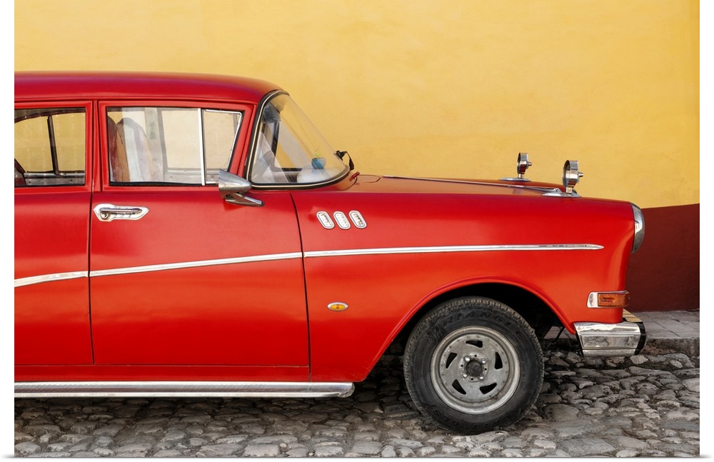 Close-up of Retro Red Car parked on a cobblestone road with a yellow and red wall in the background.