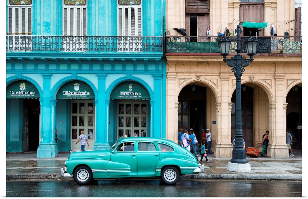 Photograph of a turquoise vintage car parked outside of a bright blue building in downtown Havana.