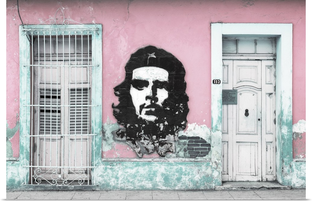 Photograph of a Cuban facade with Che Guevara painted in between a window and a door on a pink wall.