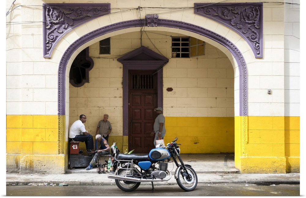 Photograph of a blue motorcycle parked along a street in Havana with pretty purple architectural details in the background.