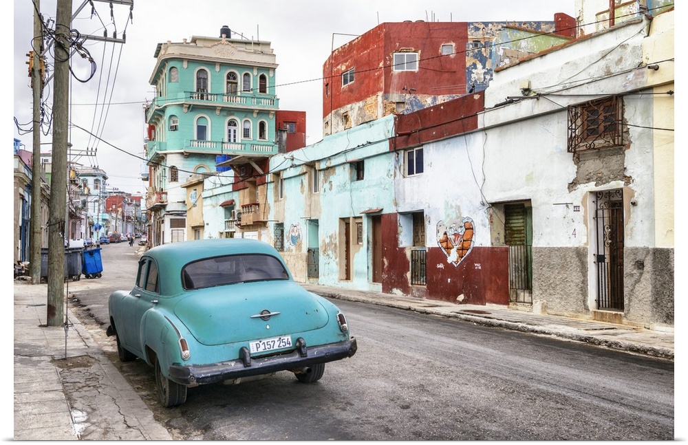 Photograph of a vintage turquoise car parked in the street surrounded by worn buildings in Havana, Cuba