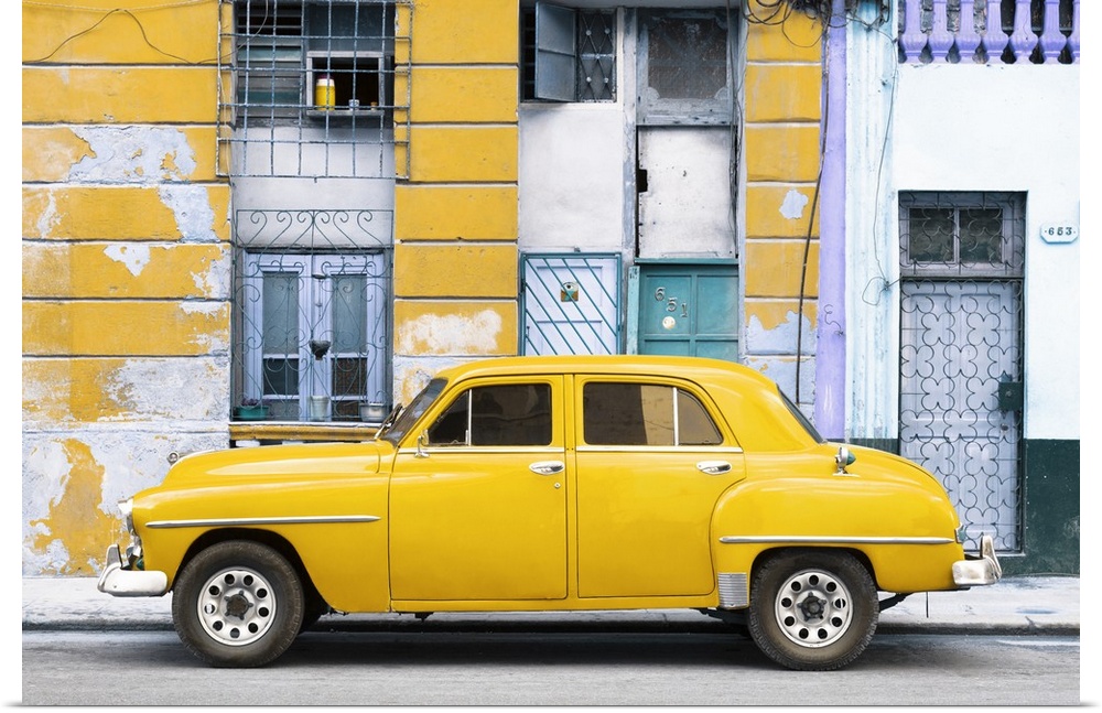 Photograph of a yellow vintage car parked on the side of a street with an old building in the background.