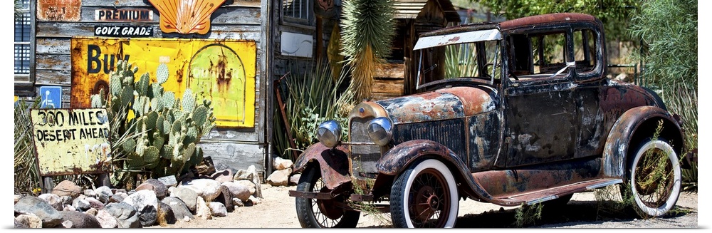A rusty antique car sits at a gas station on Route 66 among weathered old signs and cacti.