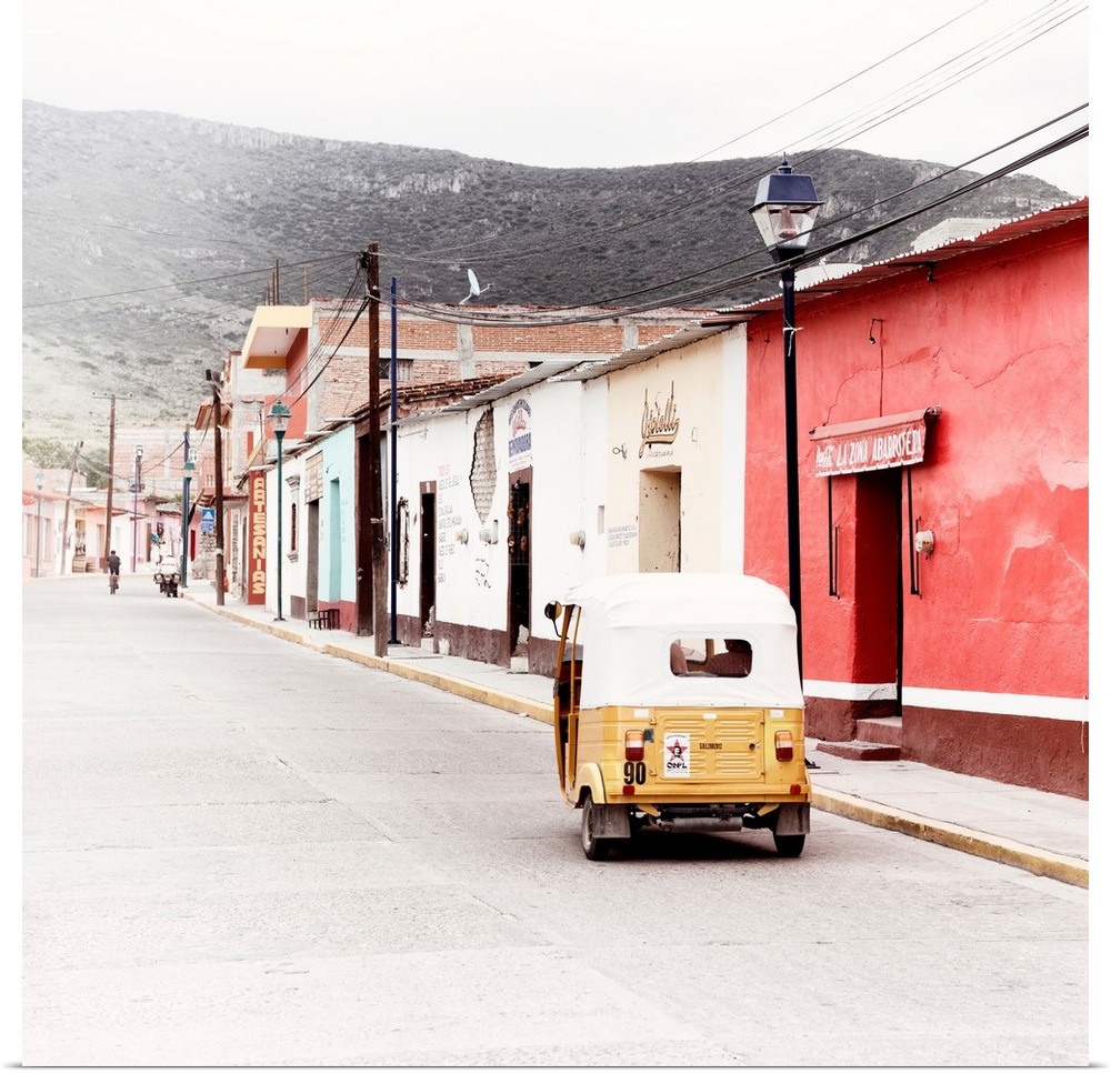 Square ashed out photograph of a Mexican street scene with a yellow Tuk Tuk on the road. From the Viva Mexico Collection.