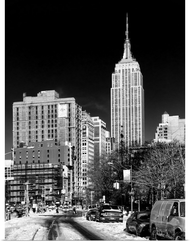A black and white photograph of the Empire state building standing tall in NYC, seen from street level.