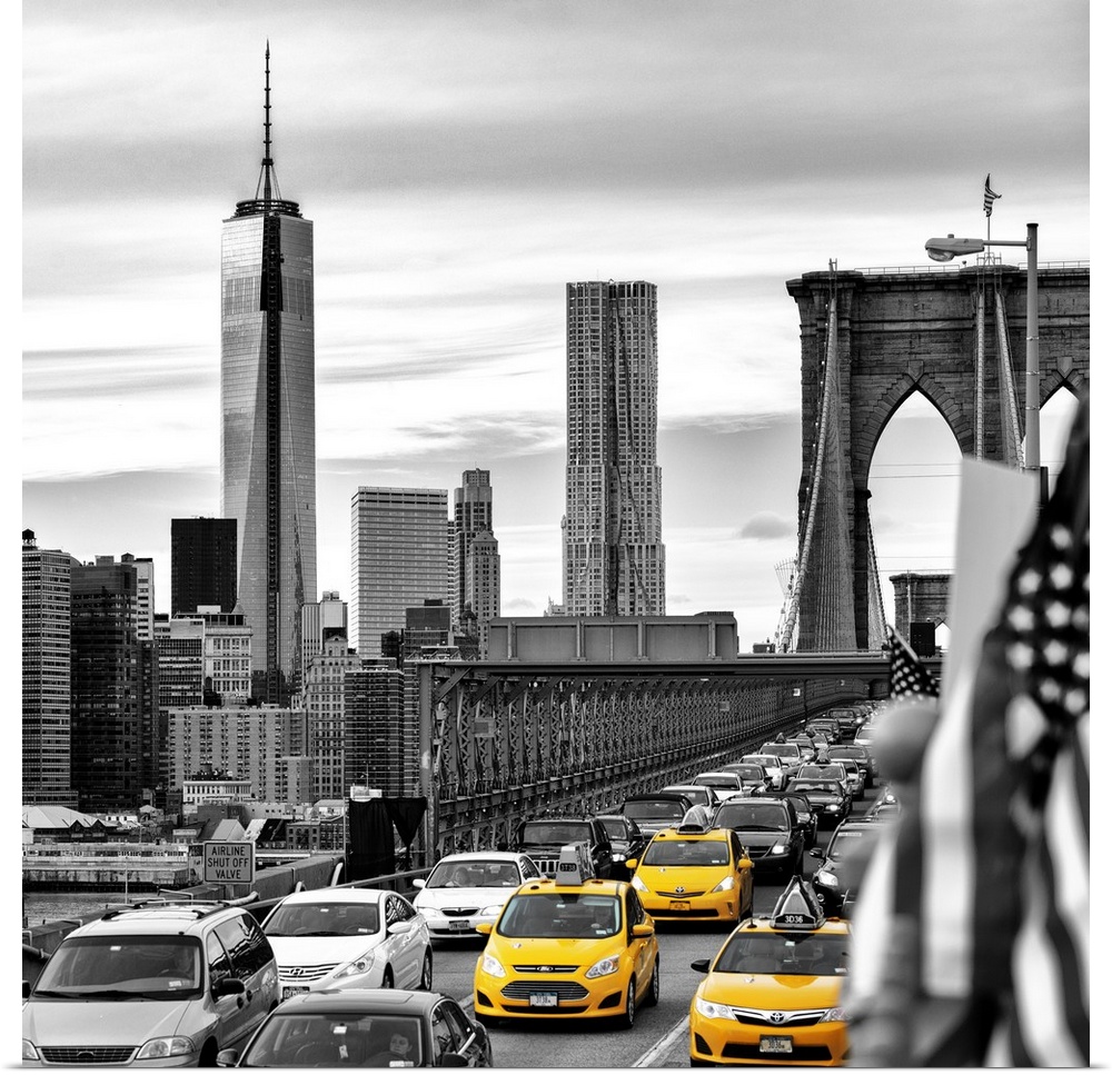 A black and white photograph of the One World Trade building from the Brooklyn bridge with yellow taxis on the bridge.