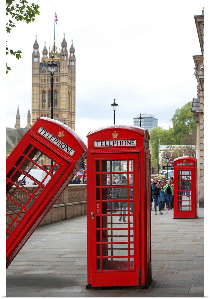 Three red phone booths, one leaning against the other, with the House of Parliament in the background.