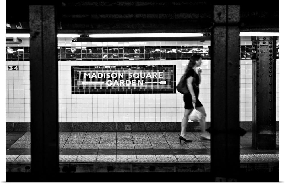 Black and white photo of a subway station at Madison Square Garden, with a woman walking past.
