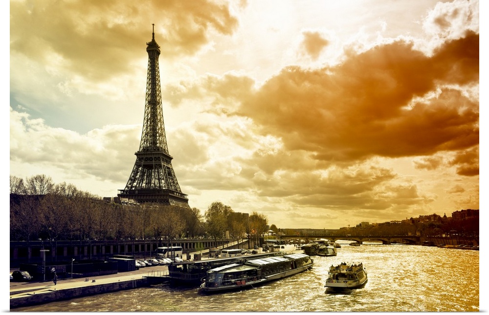 Fine art photo of the Eiffel Tower on the edge of the Seine River with dramatic lighting from the setting sun.