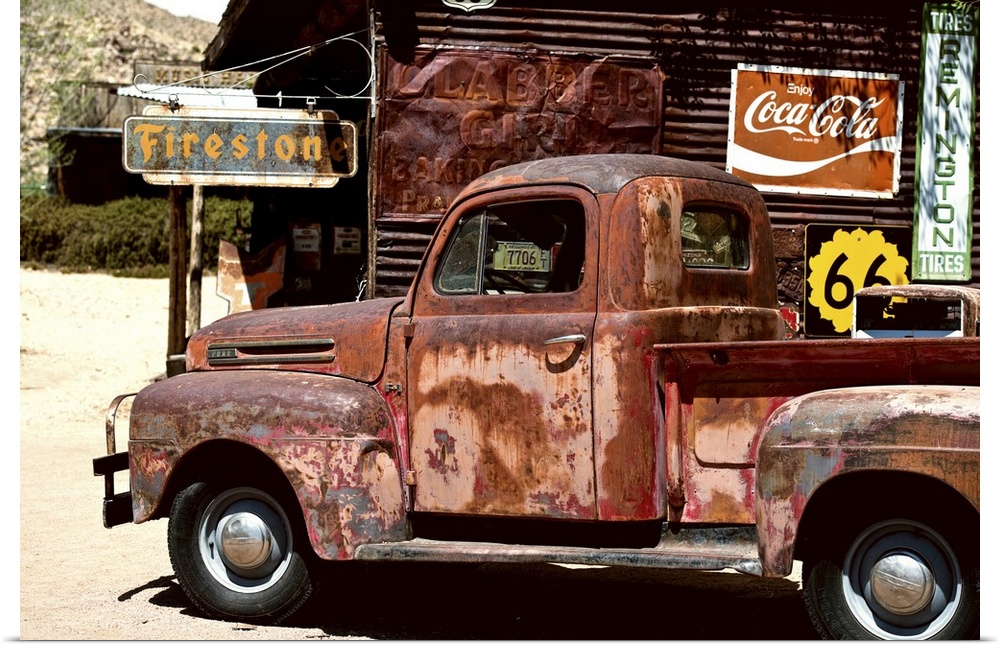 A very rusty pickup truck sits by a weathered gas station on Route 66.