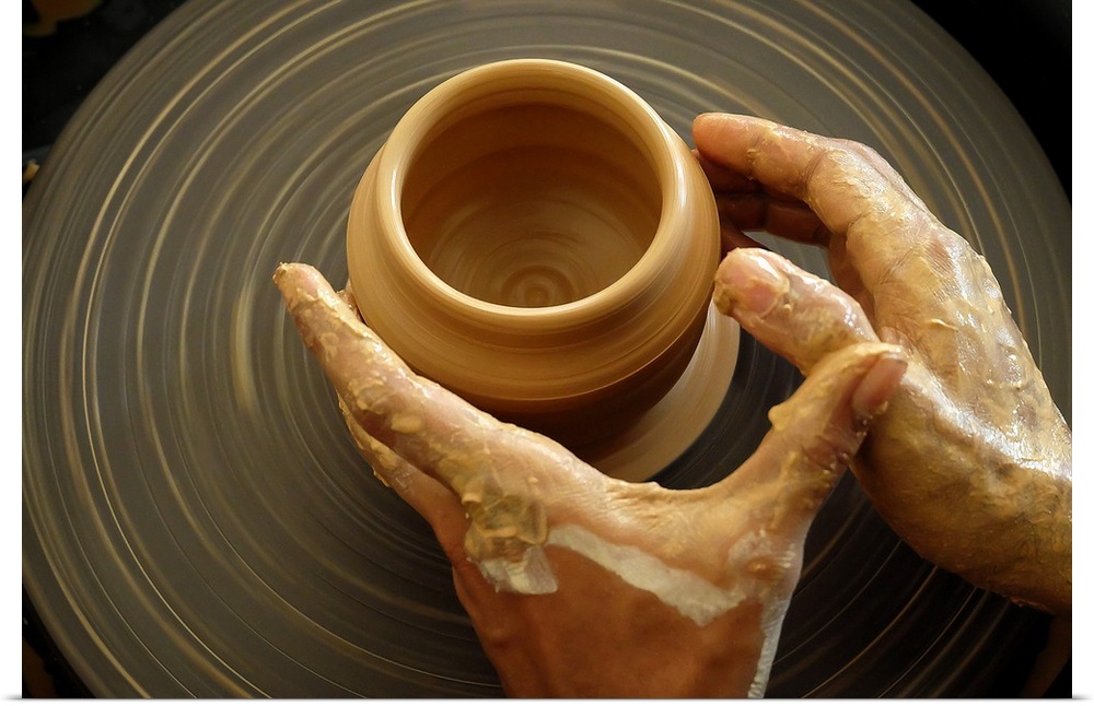 A potter shaping clay with their hands on a spinning pottery wheel.