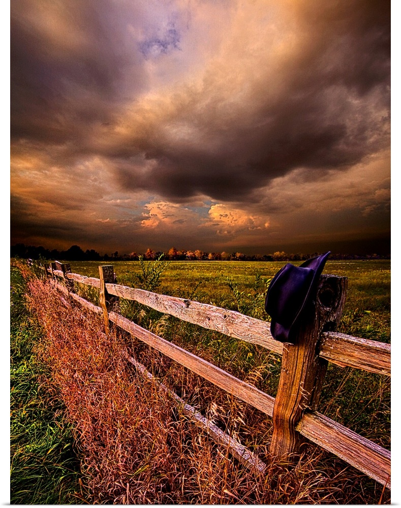 A hat resting on the post of a wooden fence under a cloudy sky.