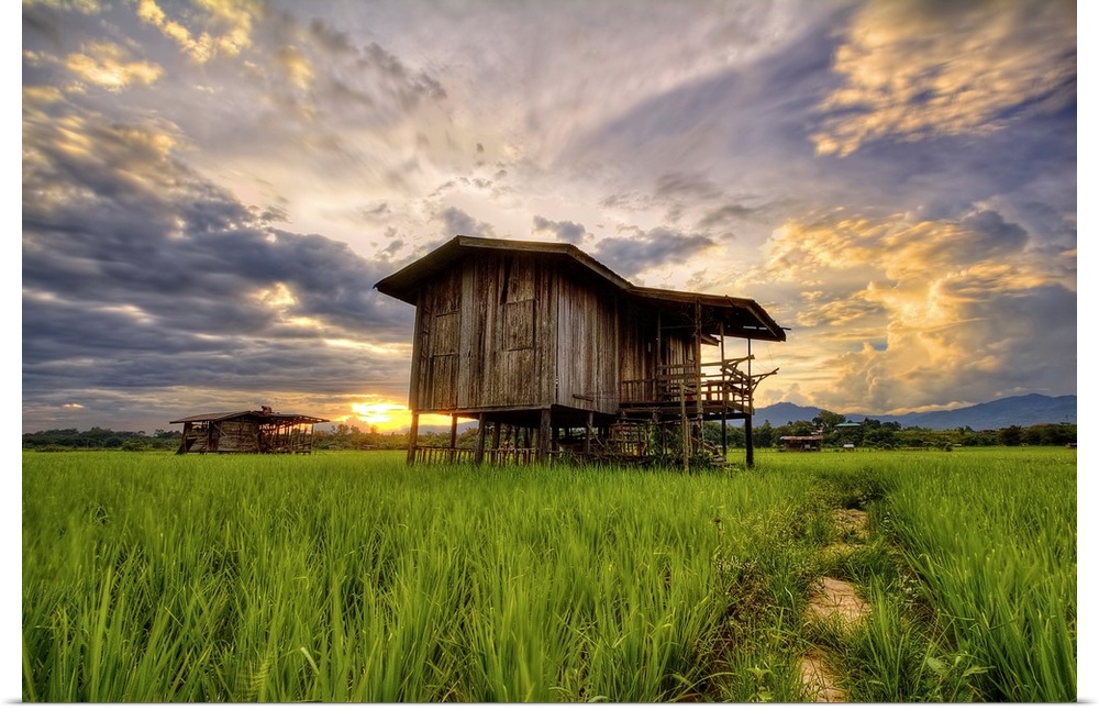 An old wooden building in a field under a colorful sunset sky.