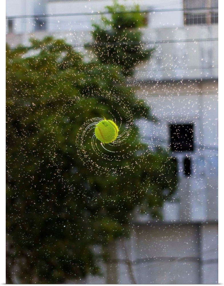 Photograph of a tennis ball spinning with water streaming off it.