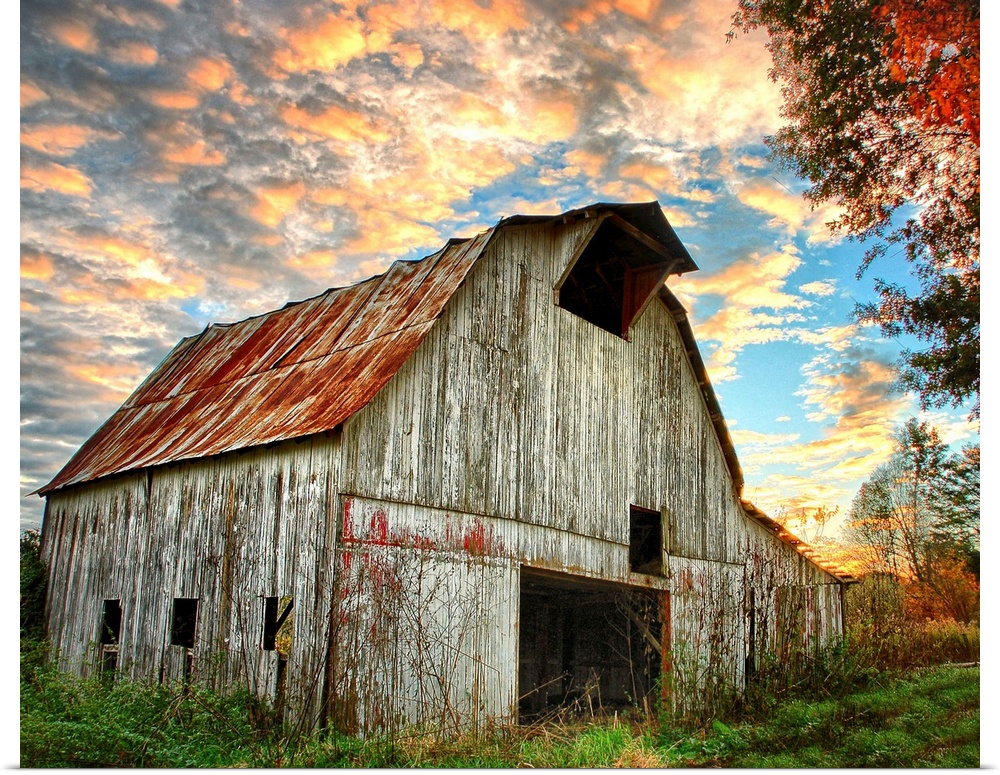 Sunset over an old, weathered barn, with a cloudy sky.