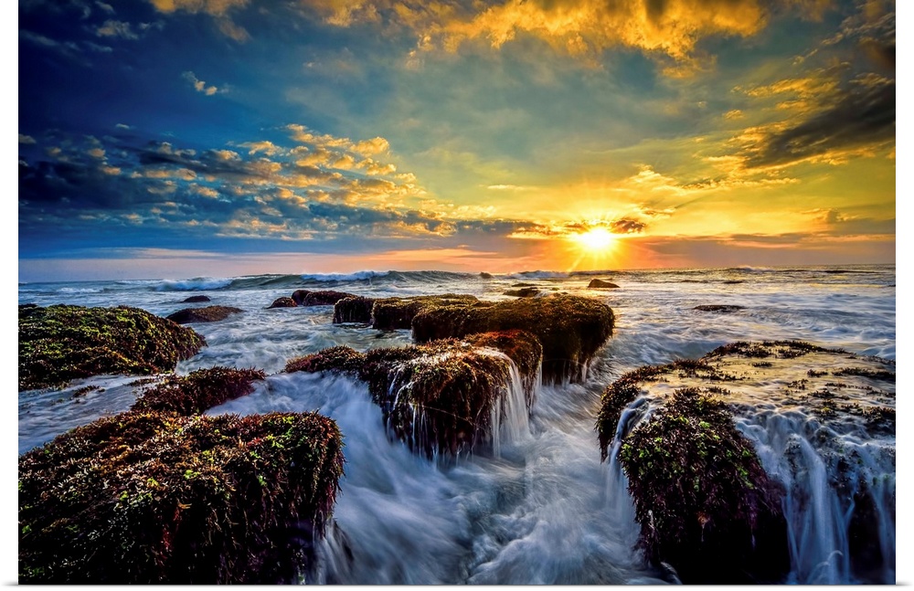 Dramatic clouds of sunset hanging over a seascape with rocky shoreline in the foreground.
