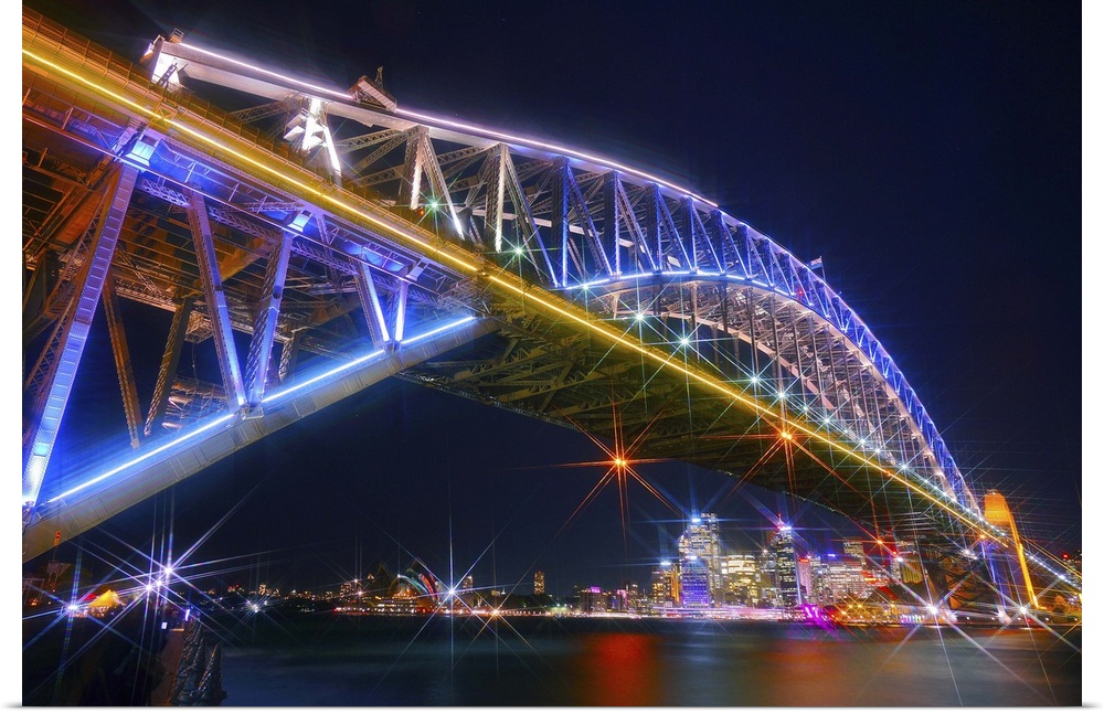 Photograph of the Sydney Harbor skyline from under the massive neon lit bridge.