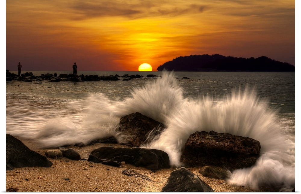 Waves crashing onto rocks on the beach at sunset.