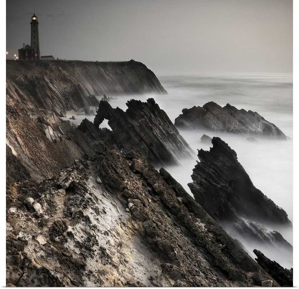 Dynamic photograph of a lighthouse on a foggy jagged rocky coast.