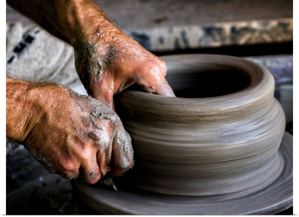 A sculptor's hands shaping a round clay pot on a spinning wheel.