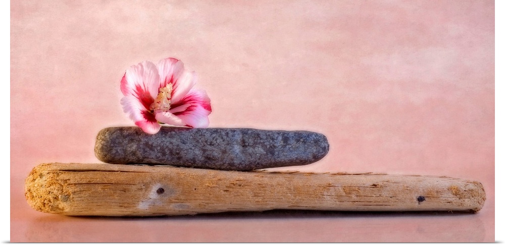 Decorative artwork that has a plank of wood with a stone on top of it and a hibiscus flower on top of the stone.