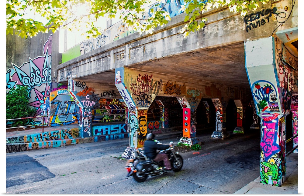 A person on a motorcycle drives past columns and sidewalks covered in colorful graffiti at the entrance of the Krog Street...