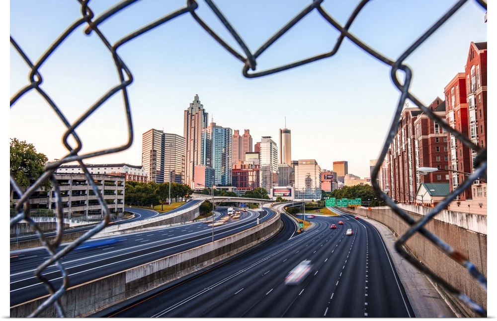The skyline of Atlanta, Georgia, seen through a hole in a chain-link fence over a busy street.