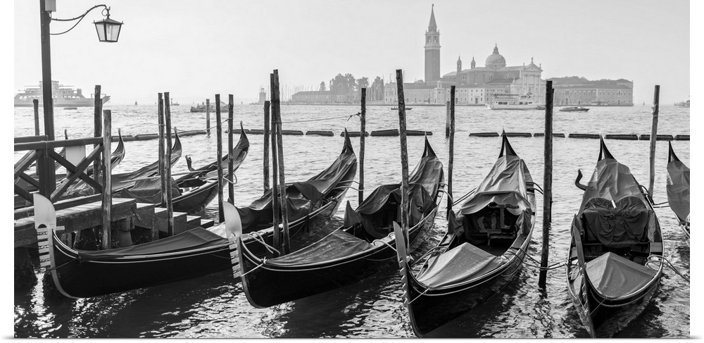 Black and white photograph of a row of gondolas in front of Piazza San Marco (St. Mark's Square) in Venice, Italy.