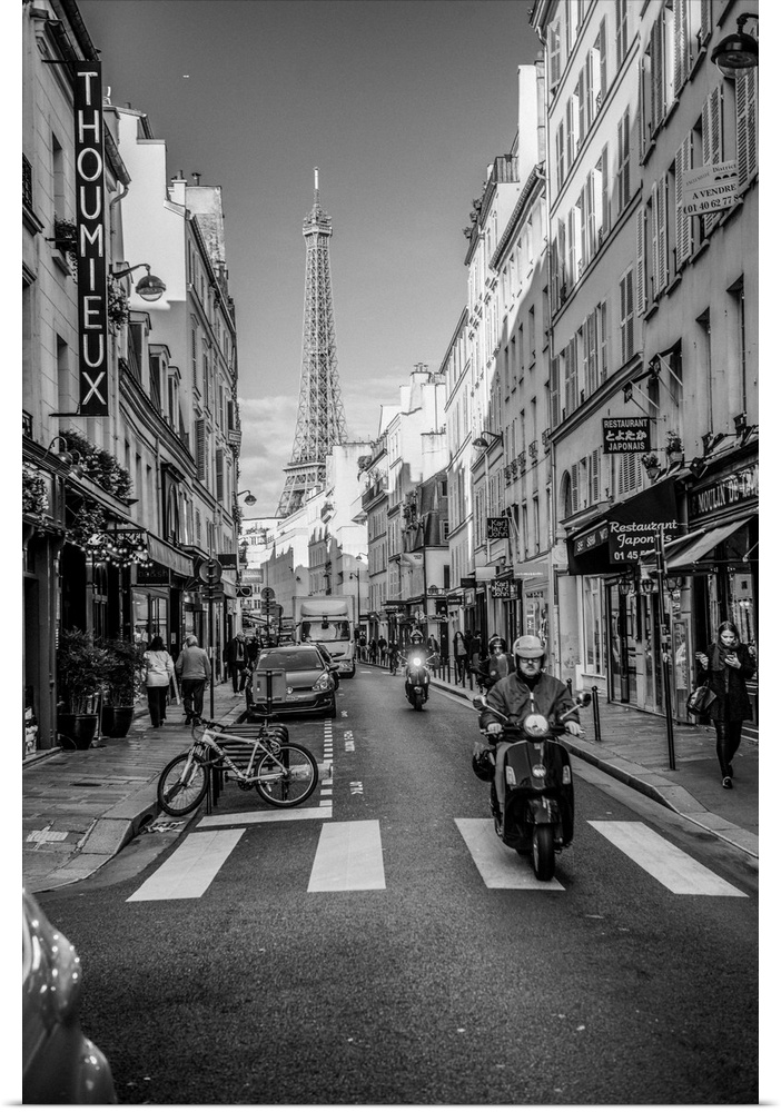 Black and white photograph of a street view in Paris with the Eiffel Tower in the background and a person on a moped in th...