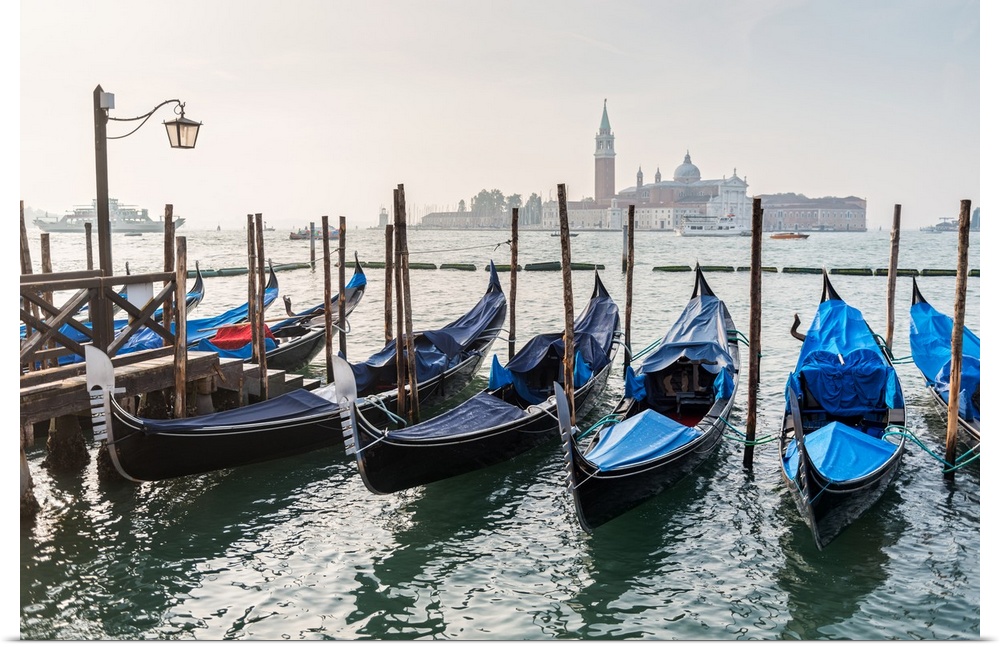 Photograph of gondolas lined up in a row with St. Mark's Square (Piazza San Marco) in the background.