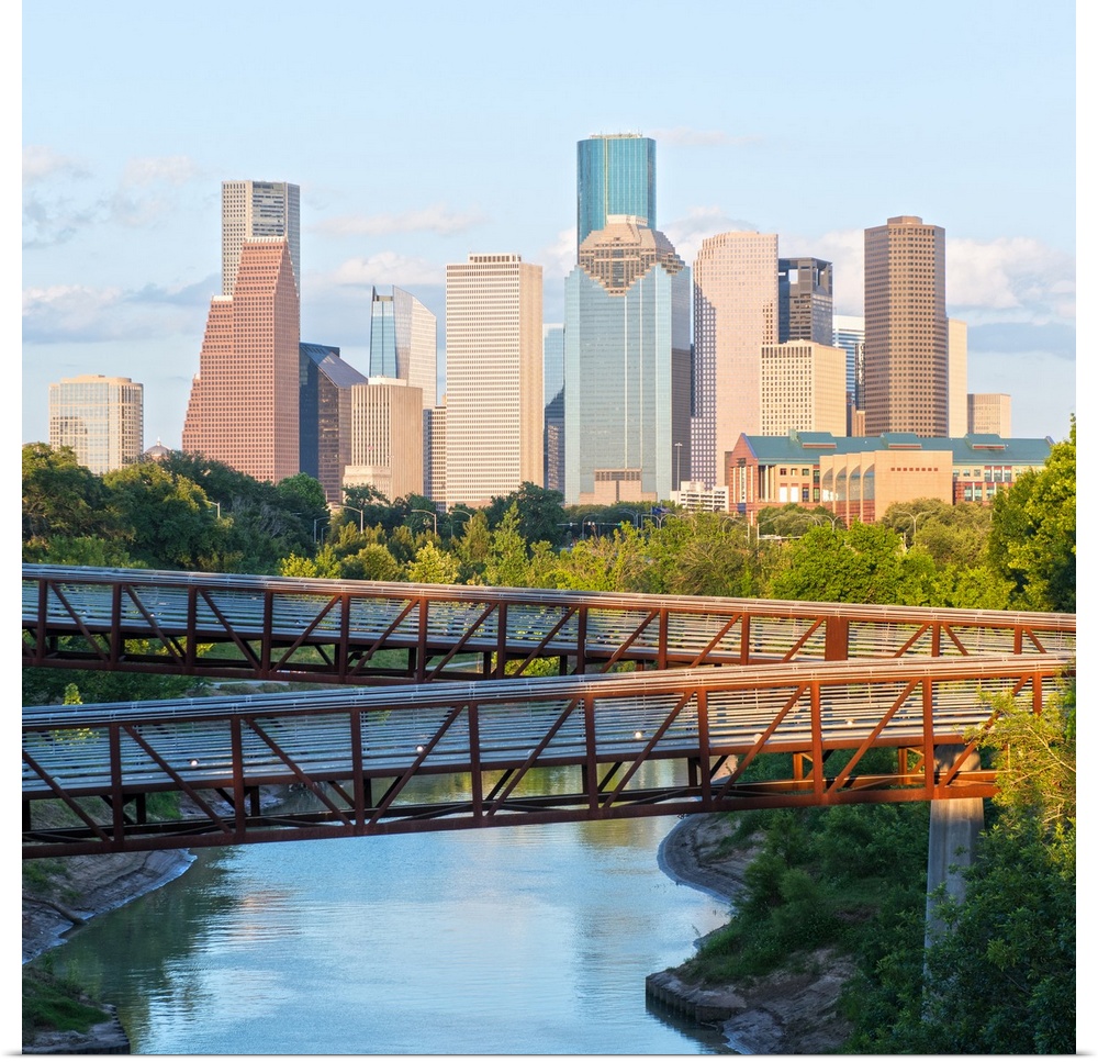 Square photograph of the Houston TX skyline in the distance with the  Rosemont pedestrian bridge in the foreground over th...