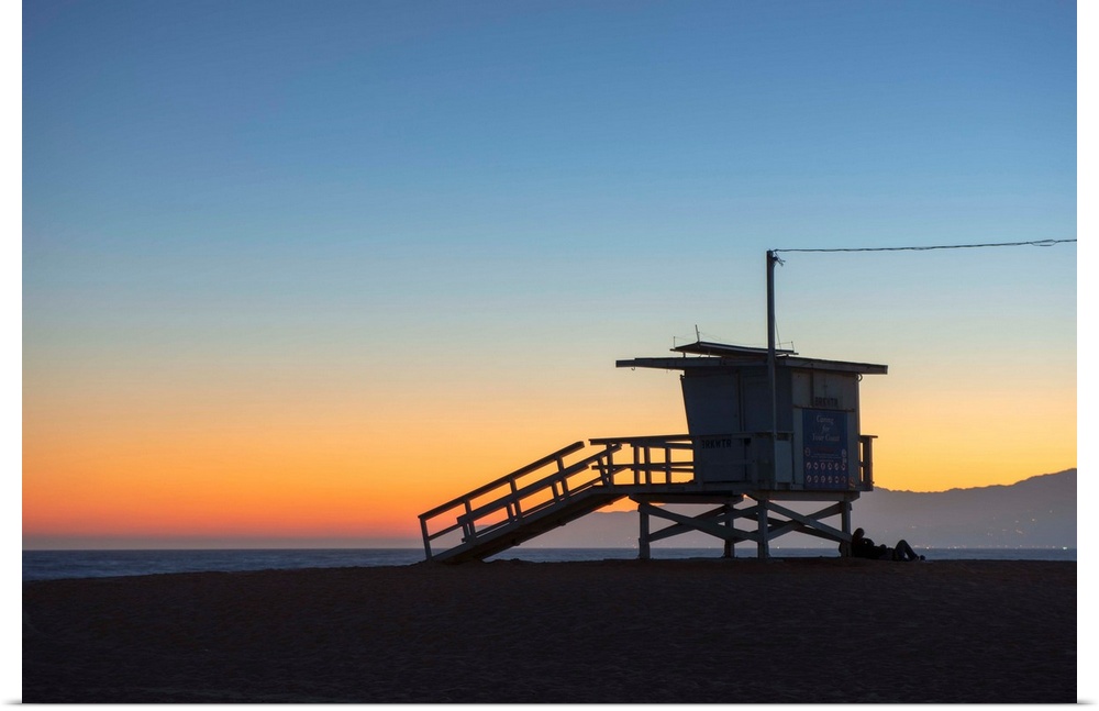 The sun sets on Venice beach with the silhouette of a lifeguard tower.